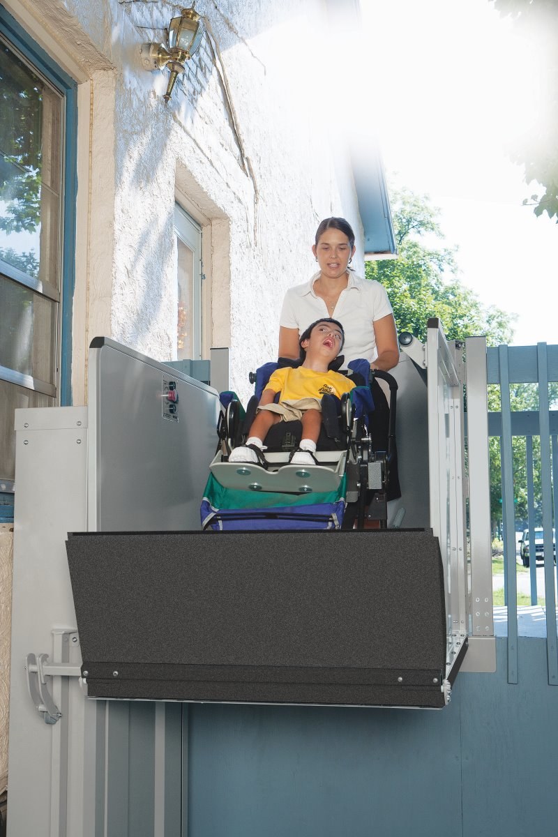 A caregiver assisting a child using a Bruno vertical platform lift at a home entrance
