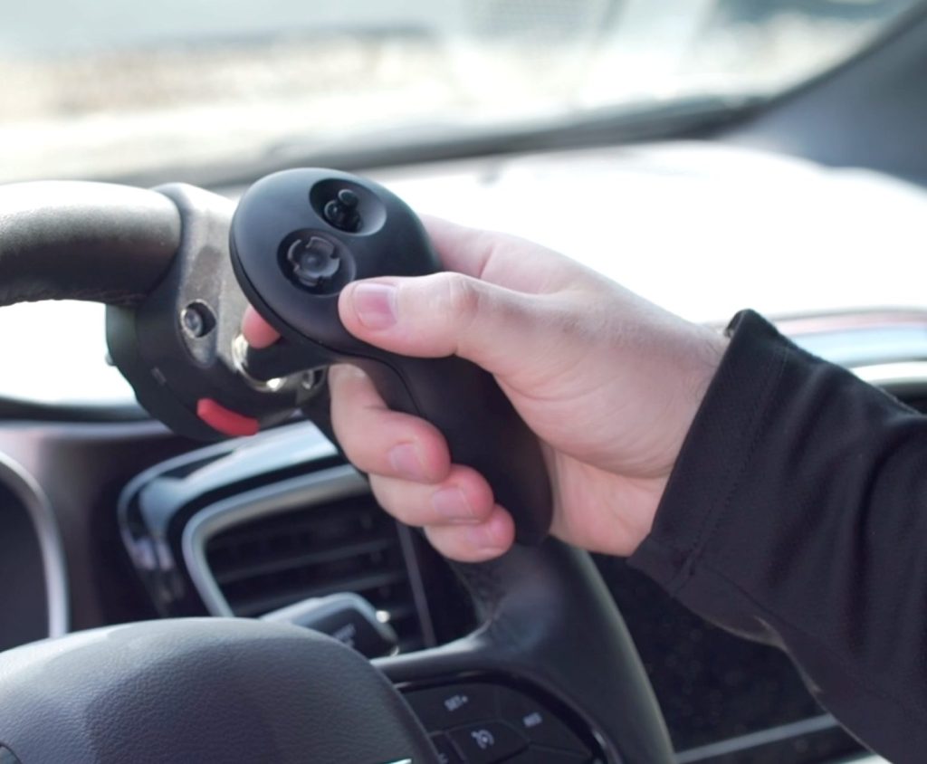A driver's hand resting on a hand-control lever mounted beside the steering wheel