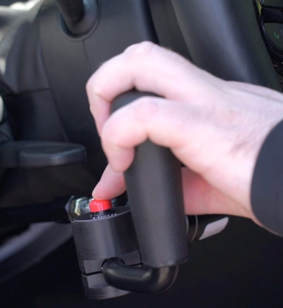 A red horn button built into the grip of a hand control, under the driver's thumb