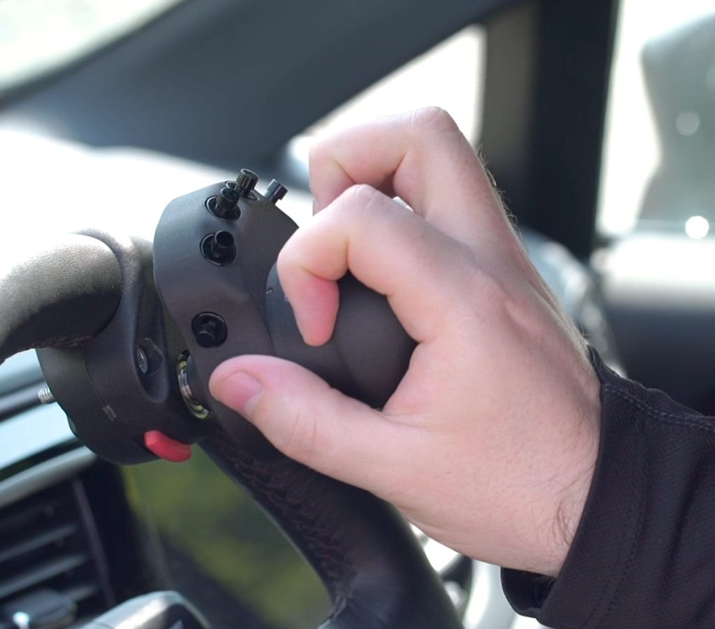 A driver's hand on a control handle with buttons for lights, indicators and wipers