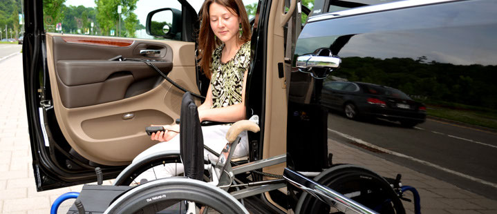 A woman beside a minivan door operating a pendant to stow a rigid manual wheelchair inside